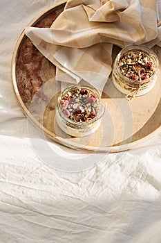 Quick healthy breakfast greek yogurt, granola with dried berries and nuts in glass jar on wooden tray on white bedding