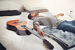 Quick nap before I start playing again. a young handsome man sleeping next to his guitar at home.