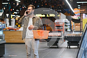 Quick text during shopping. Handsome young man holding mobile phone and smiling while standing in a food store
