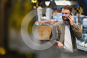 Quick text during shopping. Handsome young man holding mobile phone and smiling while standing in a food store