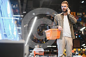 Quick text during shopping. Handsome young man holding mobile phone and smiling while standing in a food store