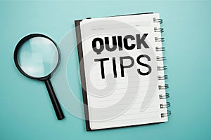 Quick Tips text message on notepad and magnifying glass flat lay on blue background
