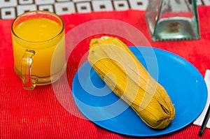 A quick but very nutritious breakfast contain a glass of orange juice and humita served on a blue dish photo