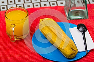 A quick but very nutritious breakfast contain a glass of orange juice and humita served on a blue dish photo
