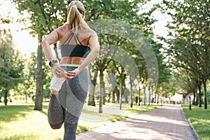 Quick warm up. Rear view of sporty woman stretching leg muscles during outdoor running workout in a green park on a