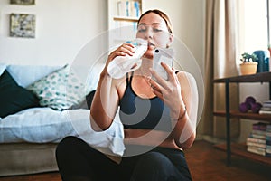 Quick water and social media break. an attractive young woman sitting and drinking water while using her cellphone after