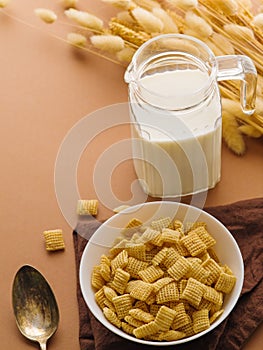 Quick whole grain breakfast - Crispy pads in a bowl, milk in a jug and a bunch of cereals on a beige background. There is an empty