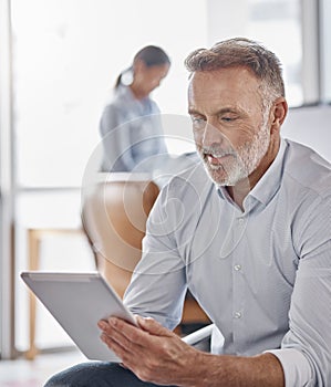 The quickest way to reach a CEO. a mature businessman using a digital tablet in a modern office.