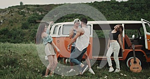 Quickly dancing group of young friends at the nature, moving charismatic, beside a retro van.
