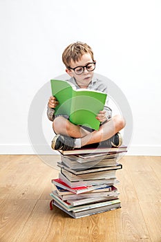 Quiet bookworm schoolboy seated on top of many books, indoor