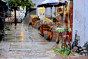Quiet and cozy deserted street cafe in the autumn rain. Old bicycle decorated with flowers.