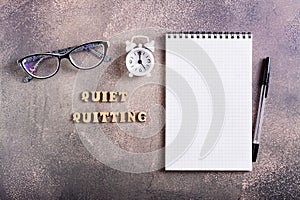 Quiet quitting concept. Notebook, pen, glasses, alarm clock and wooden letters. Top view