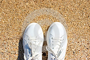 Quiet surf, yellow sand and white sneakers closeup