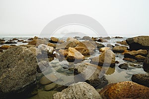 Quiet water, seashore rocks, and silhouette of vessel on a horizon at an overcast day, Morro Bay, CA