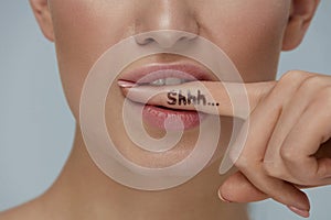 Quiet! Woman`s face with shhh on finger in mouth. Secret gossip photo