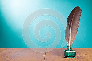 Quill ink pen with inkwell on wooden table front gradient mint green background. Vintage style photo