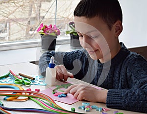 Quilling technique. Boy making decorations or greeting card. Paper strips, flower, scissors. Handmade crafts on holiday: Birthday,