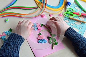 Quilling technique. Boy making decorations or greeting card. Paper strips, flower, scissors. Handmade crafts on holiday: Birthday,