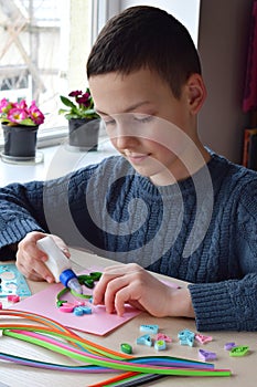 Quilling technique. Boy making decorations or greeting card. Paper strips, flower, scissors. Handmade crafts on holiday: Birthday