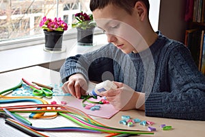 Quilling technique. Boy making decorations or greeting card. Paper strips, flower, scissors. Handmade crafts on holiday: Birthday