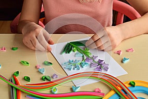 Quilling technique. Girl making decorations or greeting card. Paper strips, flower, scissors. Handmade crafts on holiday: Birthday