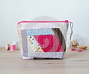 Quilted patchwork notions bag, glass jar, pins and thread spools on wooden desk
