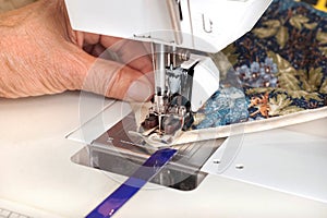Quilter sewing on binding to quilt.