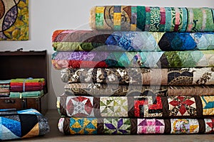 Quilts stacked and wooden chest with stacks of fat quarters on white wall background