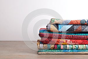 Quilts stacked on wooden table on white wall background