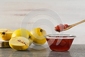 Quince jam in glass bowl with ripe fresh quinces on rustic table