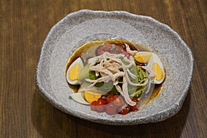 quinoa avocado slice, shredded chicken, boiled egg silce, tomatos slice on white and black ceramic bowl on wooden table background