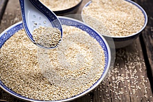 Quinoa in bowl with spoon on wooden background.