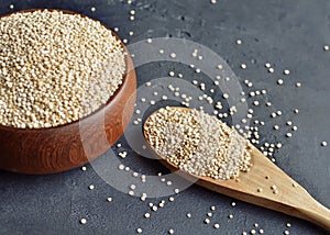 Quinoa in a brown wooden bowl and spoon on dark stone background. Dry uncooked cereal grains, cooking ingredient