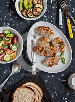 Quinoa crusted chicken, vegetable salad, grilled eggplant and pepper - dinner table. On a dark background