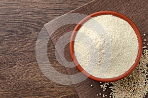 Quinoa flour in bowl and seeds on wooden table, top view. Space for text
