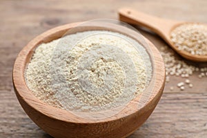 Quinoa flour in bowl and spoon with seeds on wooden table, closeup