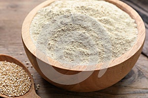 Quinoa flour in bowl and spoon with seeds on wooden table, closeup