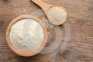 Quinoa flour in bowl and spoon with seeds on wooden table, flat lay