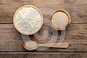 Quinoa flour in bowls and spoon with seeds on wooden table, flat lay