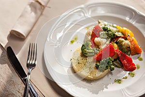 Quinoa with herbs and steamed vegetable in an oval white plate on an old wooden table. in the rays of the bright sun