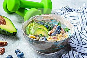 Quinoa salad with berries, avocado and nuts, dumbbells on the background. Healthy post-workout food