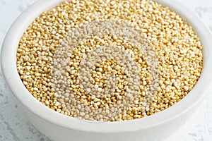 Quinoa seed in white bowl on white background. Dried cereals in cup, vegan food, fodmap diet. Side view, close up