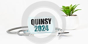 QUINSY 2024 word on notebook, stethoscope and green plant