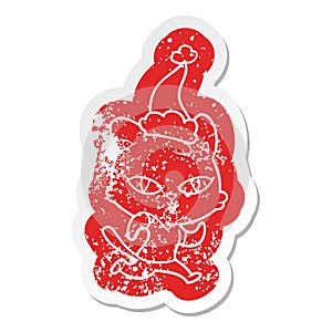 quirky cartoon distressed sticker of a cat out for a run wearing santa hat