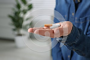 Quitting smoking concept. Woman holding broken cigarette on blurred background, closeup. Space for text