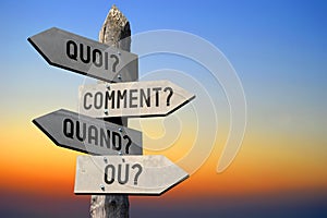 Quoi?, comment?, quand?, ou? - French / what? how? when? where? - English - wooden signpost, sunset sky