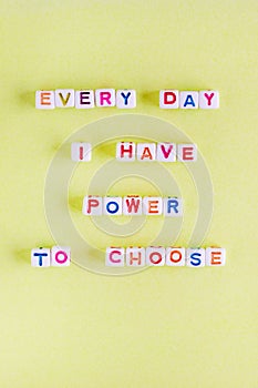 Quote `Every day I have power to choose` made out of beads on pastel yellow background