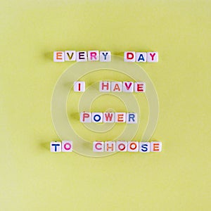 Quote `Every day I have power to choose` made out of beads on pastel yellow background