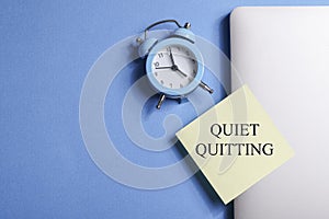 quote 'Quiet quitting' on yellow sticker on computer with clock