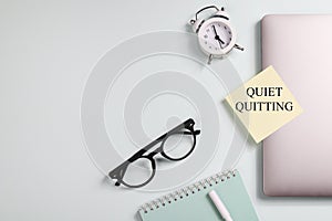 quote 'Quiet quitting' on yellow sticker on computer with clock and notebook.